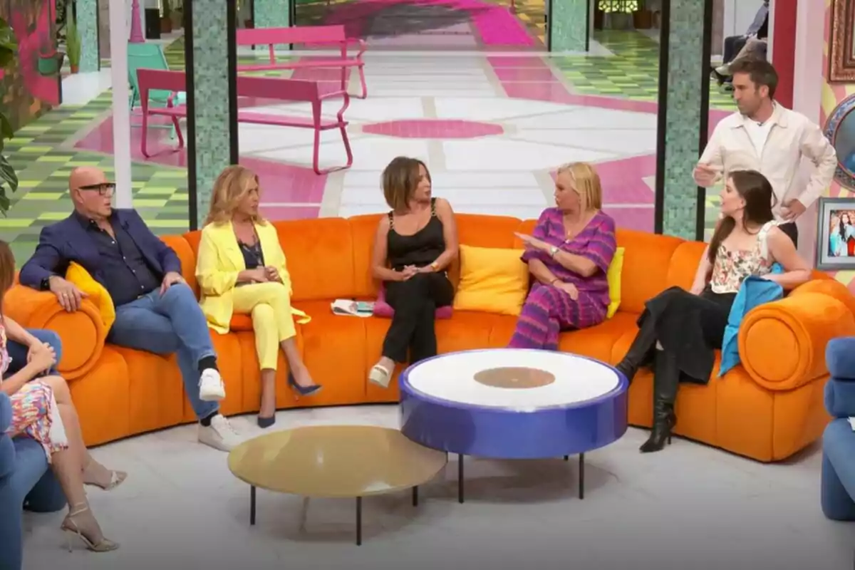 Un grup de persones format per Kiko Matamoros, Lydia Lozano, María Patiño, Belén Esteban, Inés Hernand i Aitor Albizua està assegut en un sofà taronja en un plató de televisió de La Família de la Tele acolorit, conversant entre ells mentre un home dret sembla estar parlant.