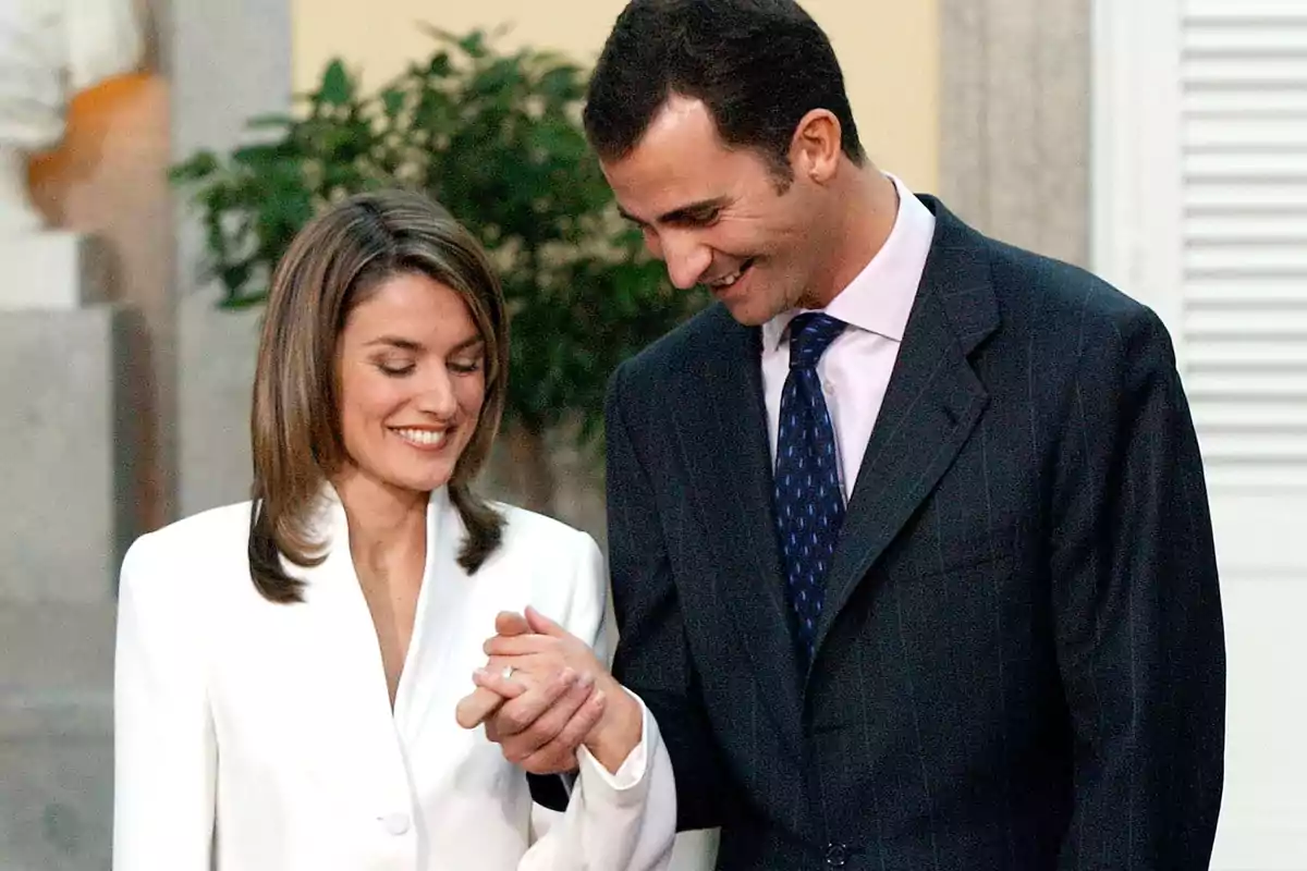 Queen Letizia and King Felipe VI smile at each other while holding hands in a formal setting. Queen Letizia and King Felipe VI smile at each other while holding hands in a formal setting.