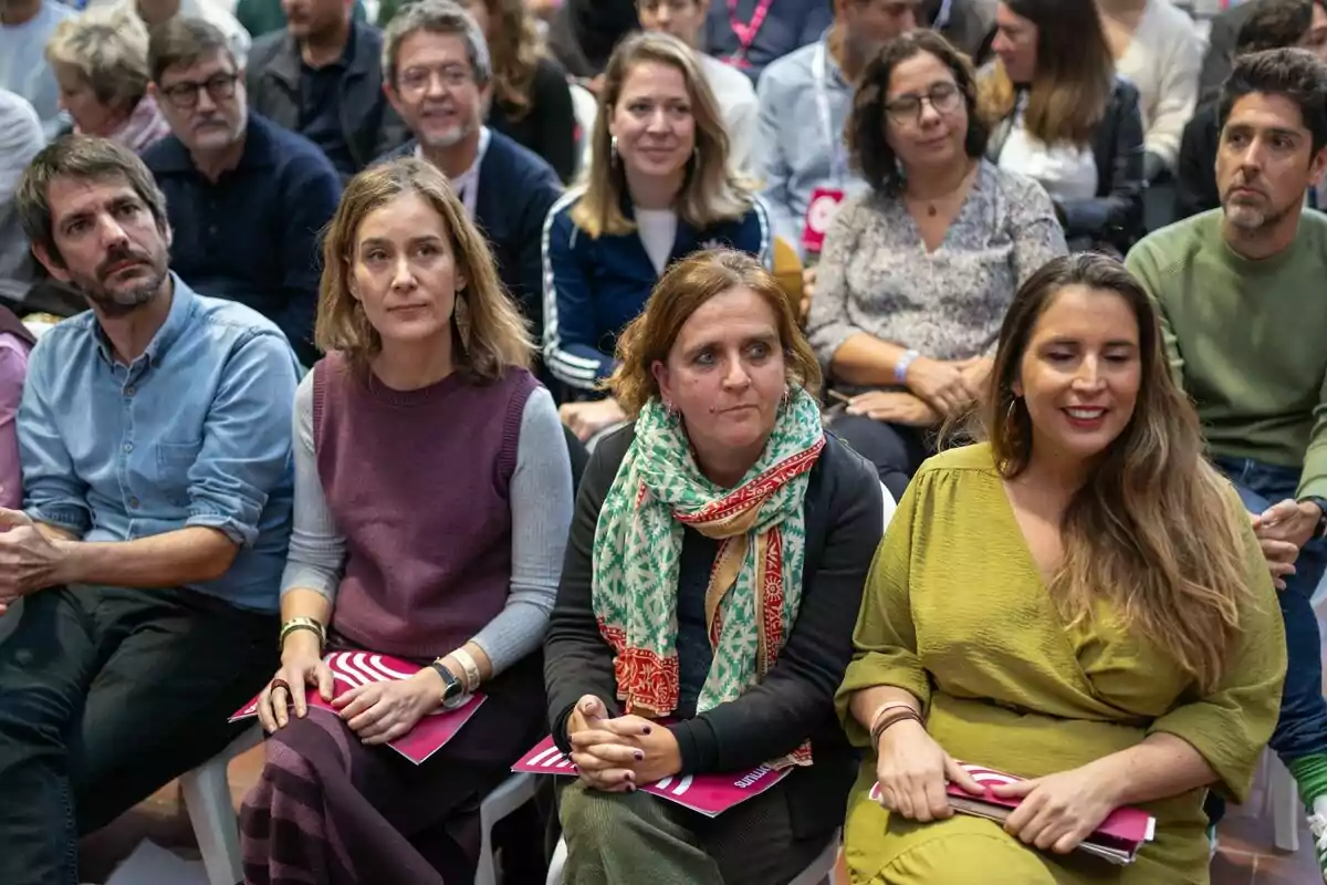 Un grup de persones assegudes en un esdeveniment, algunes sostenint fulletons.