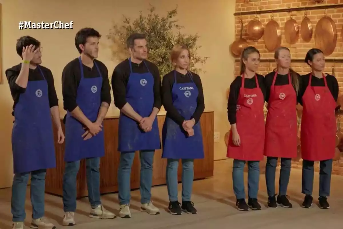 Sis persones amb davantals de color blau i vermell estan formant dos equips dins d’una cuina amb decoració de coure i el logotip de MasterChef apareix a la cantonada superior esquerra. Sis persones amb davantals de color blau i vermell estan formant dos equips dins d’una cuina amb decoració de coure i el logotip de MasterChef apareix a la cantonada superior esquerra.
