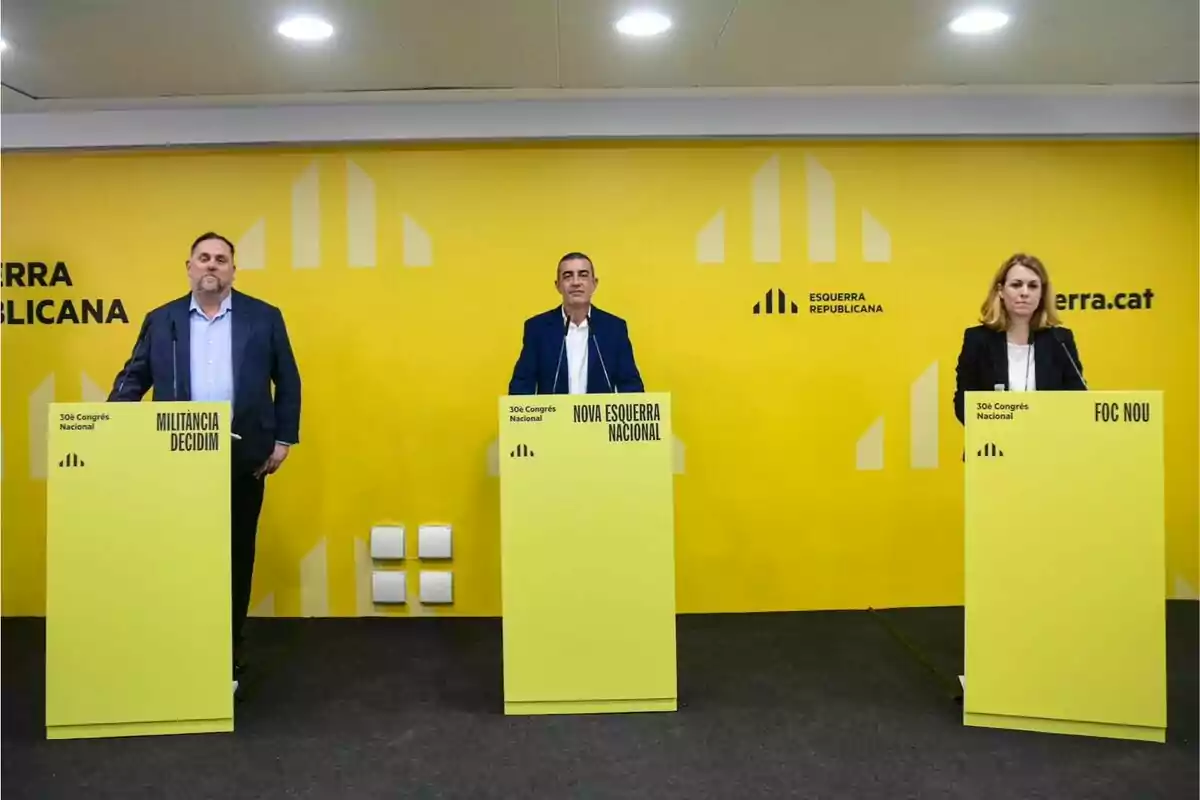 Tres persones de peu darrere de faristols grocs en un esdeveniment d'Esquerra Republicana amb un fons groc.