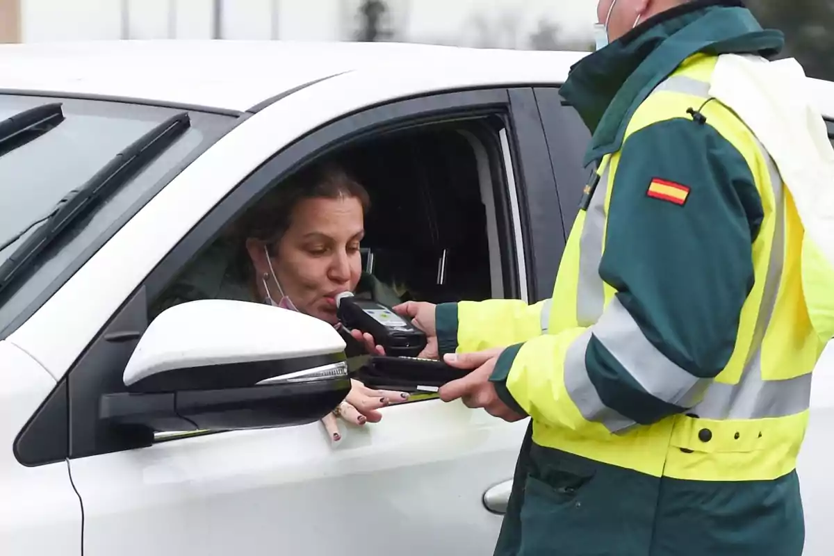 Una mujer en un coche blanco sopla en un alcoholímetro sostenido por un agente de tráfico con uniforme de alta visibilidad.