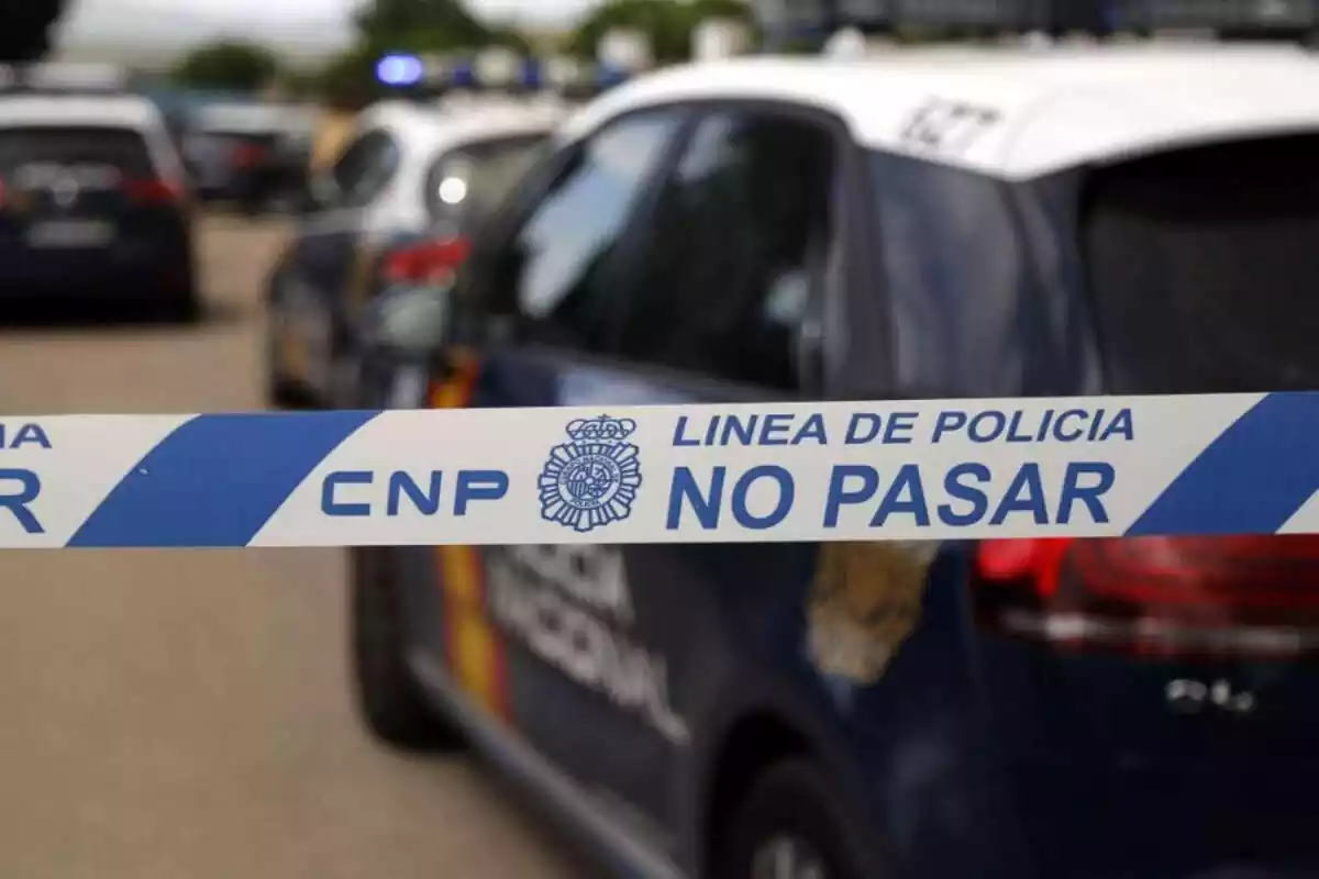 Cordó del Cos de Policia Nacional que indica 'no passar' amb un cotxe del cos de fons