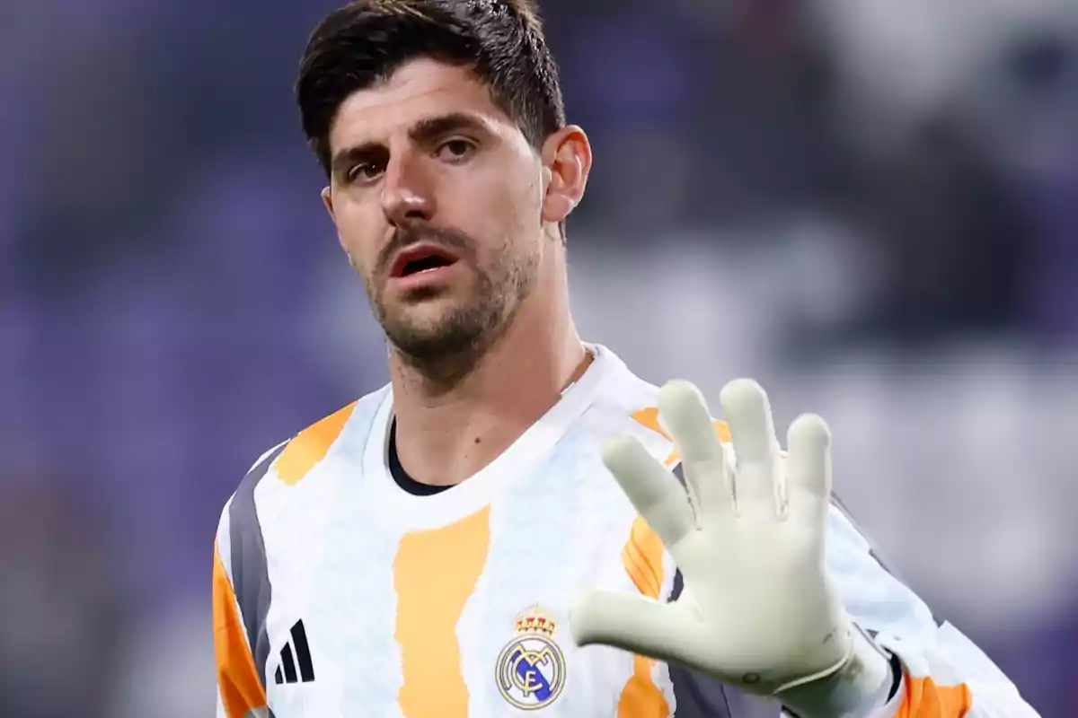 A player in a Real Madrid goalkeeper uniform raises his hand with a white glove.