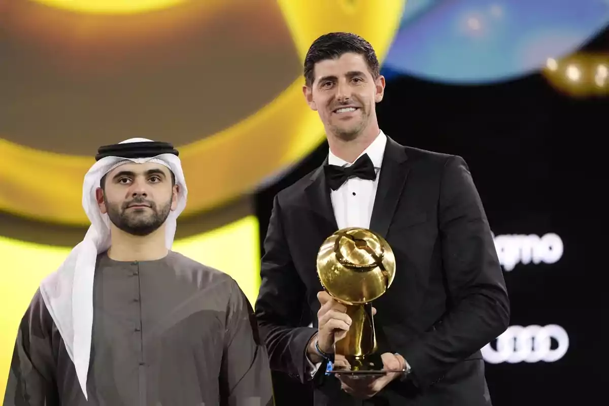 Two men pose at a formal event, one of them holding a golden trophy.