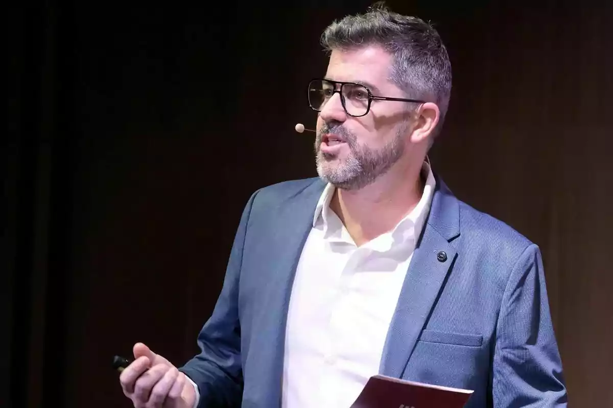 Cristian Trepat amb ulleres i barba fent servir un micròfon de diadema mentre fa una presentació de 3Cat Cristian Trepat amb ulleres i barba fent servir un micròfon de diadema mentre fa una presentació de 3Cat