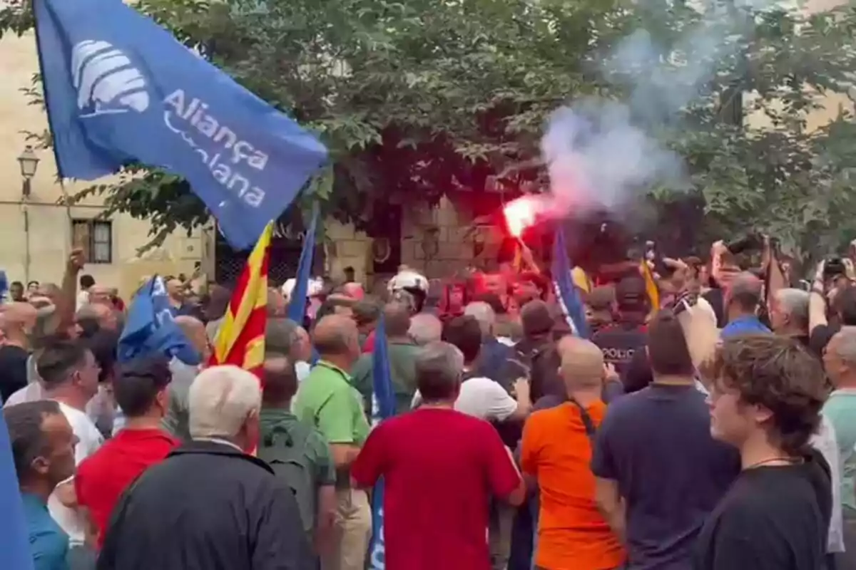 Una multitud de persones s'han reunit en una manifestació, algunes portant banderes i bengales enceses.