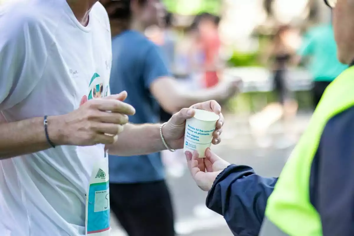 Persona entregando un vaso de agua a un corredor durante una carrera. Persona entregando un vaso de agua a un corredor durante una carrera.
