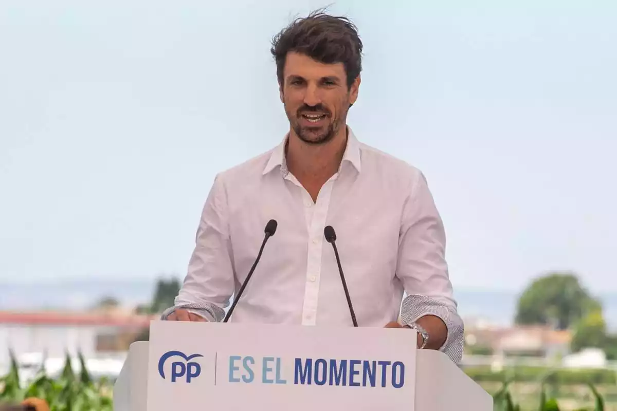 Plànol mitjà de Dante Pérez amb camisa blanca parlant des d'un faristol amb el lema 'És el moment' i el logo del PP