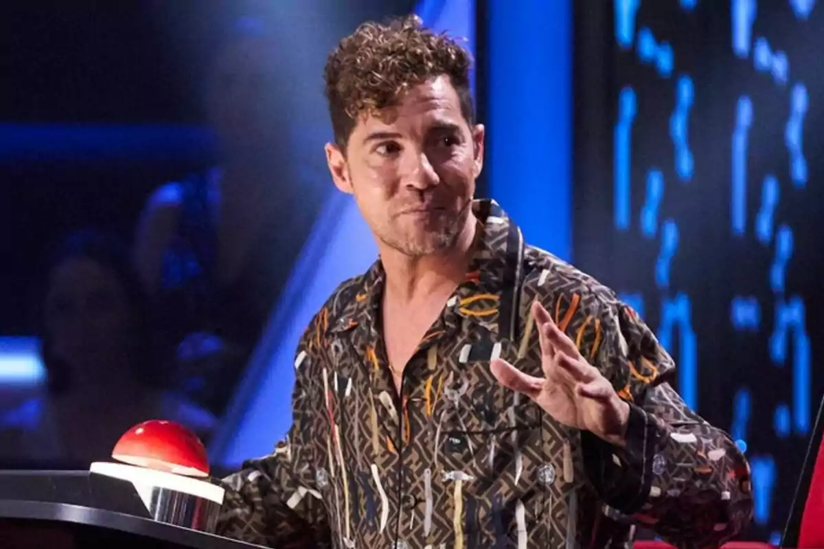 David Bisbal amb camisa estampada assegut davant d’un botó vermell en un plató de televisió de La Voz Kids