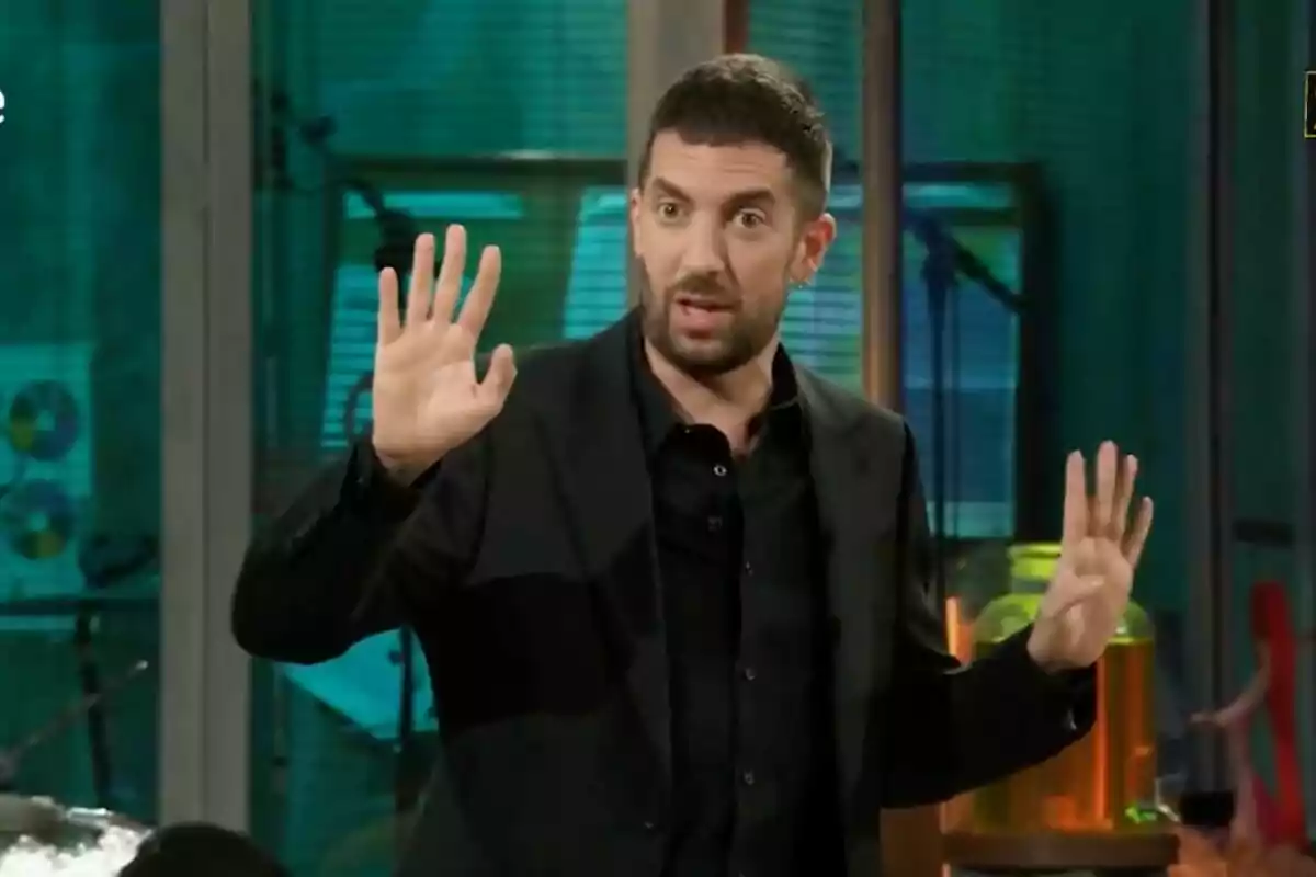 David Broncano amb barba i cabell curt, vestit amb un vestit fosc, aixeca ambdues mans amb els dits estesos en un gest expressiu, mentre es troba en un entorn interior amb llums i objectes de fons a 'La Revuelta'. David Broncano amb barba i cabell curt, vestit amb un vestit fosc, aixeca ambdues mans amb els dits estesos en un gest expressiu, mentre es troba en un entorn interior amb llums i objectes de fons a 'La Revuelta'.