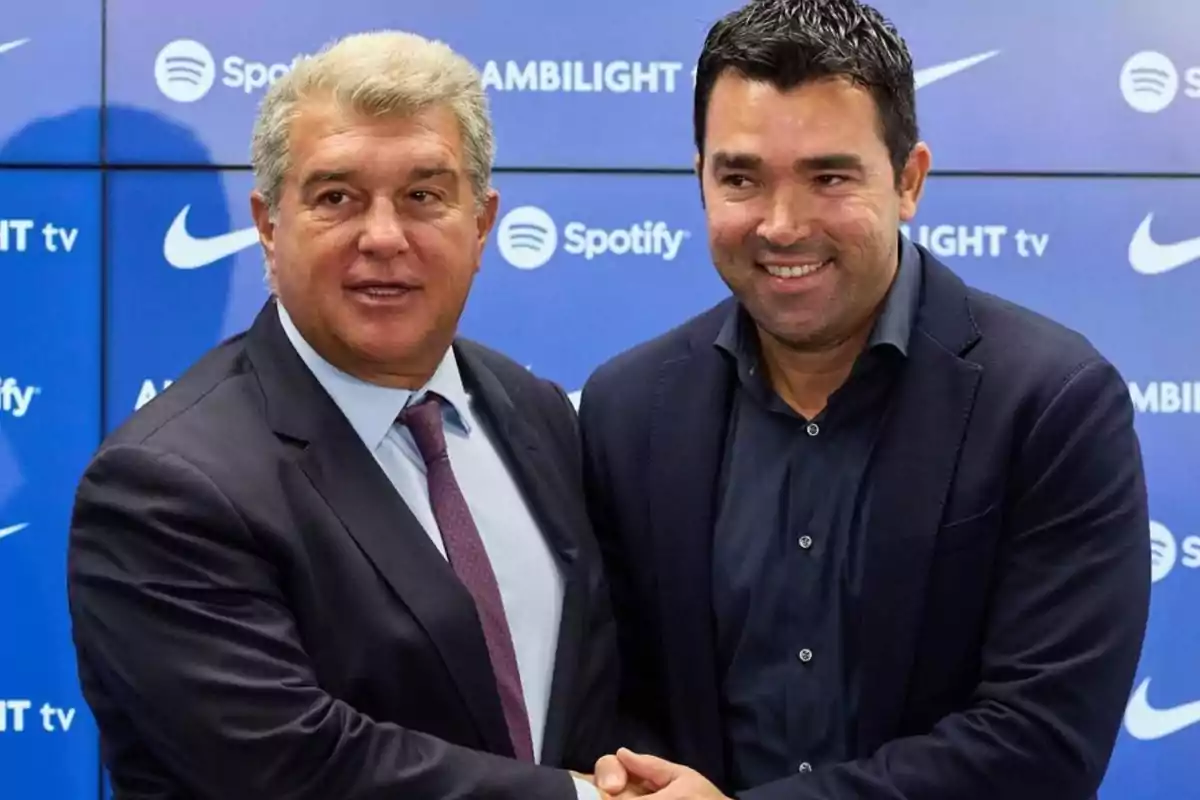 Two men in suits shake hands in front of a blue background with brand logos.