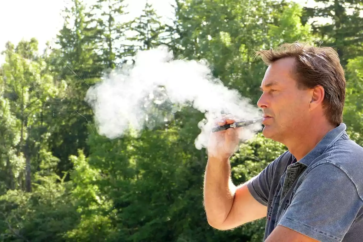 Man using an electronic cigarette outdoors with trees in the background.