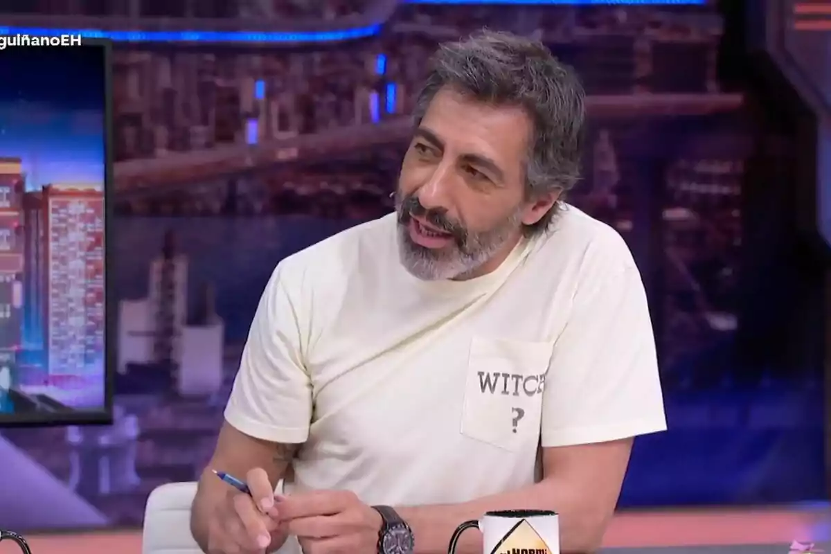Juan del Val amb cabell i barba canosos assegut a 'El Hormiguero', porta una samarreta clara amb la paraula WITCH i un signe d'interrogació a la butxaca, sosté un bolígraf i una tassa és sobre la taula davant seu.