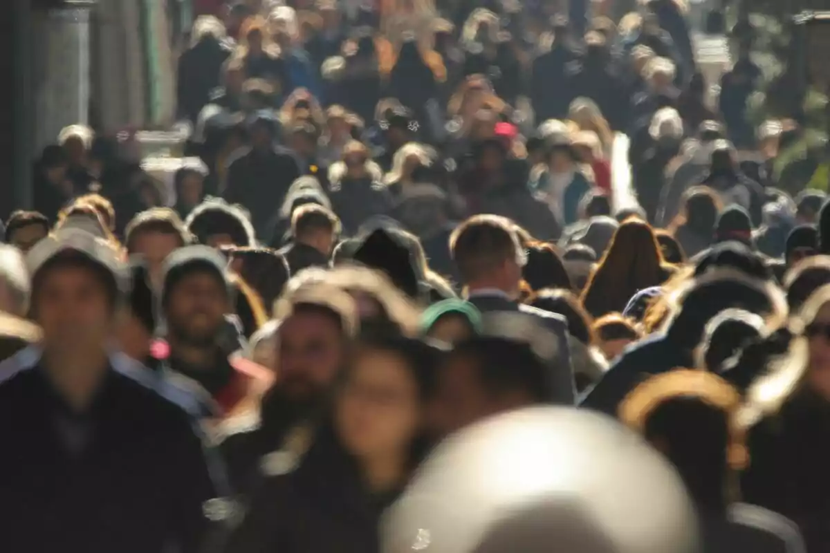 Una multitud de persones caminant per un carrer concorregut en un dia assolellat.