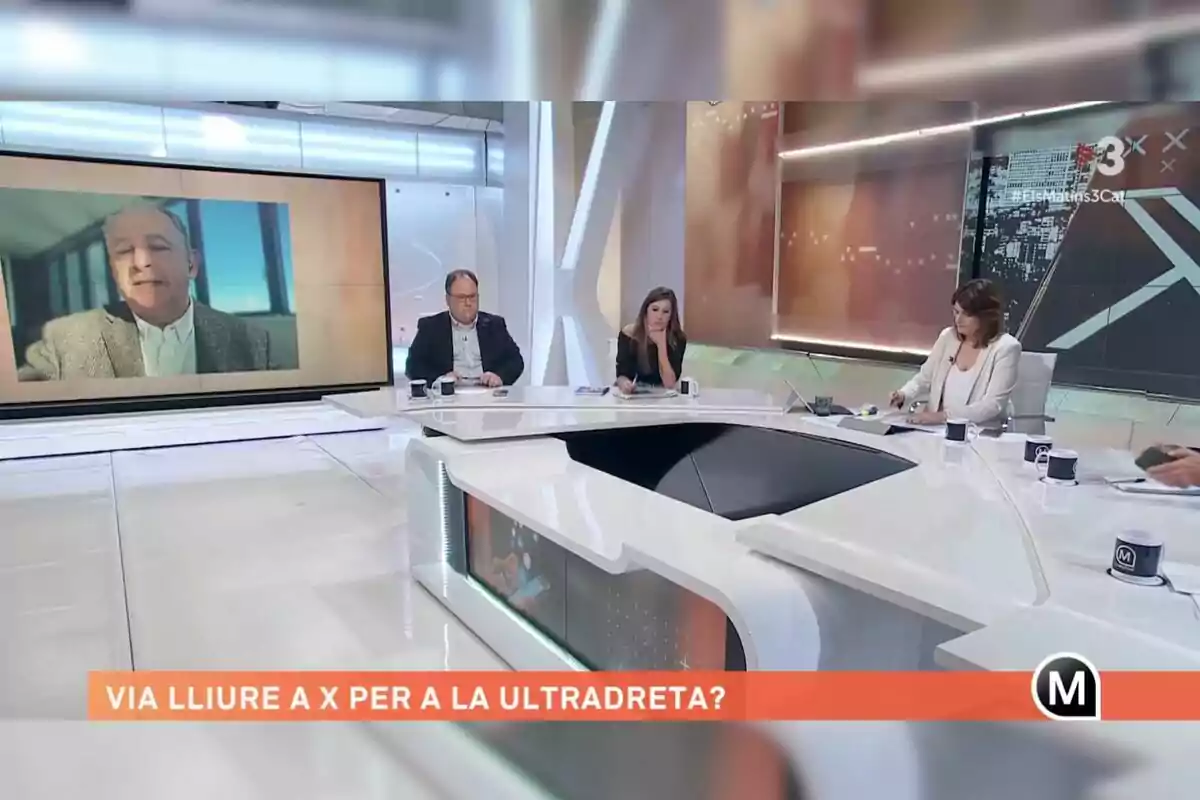 Un grup de persones participa en un programa de televisió en un estudi modern, amb una pantalla gran mostrant un home i un text en català a la part inferior.