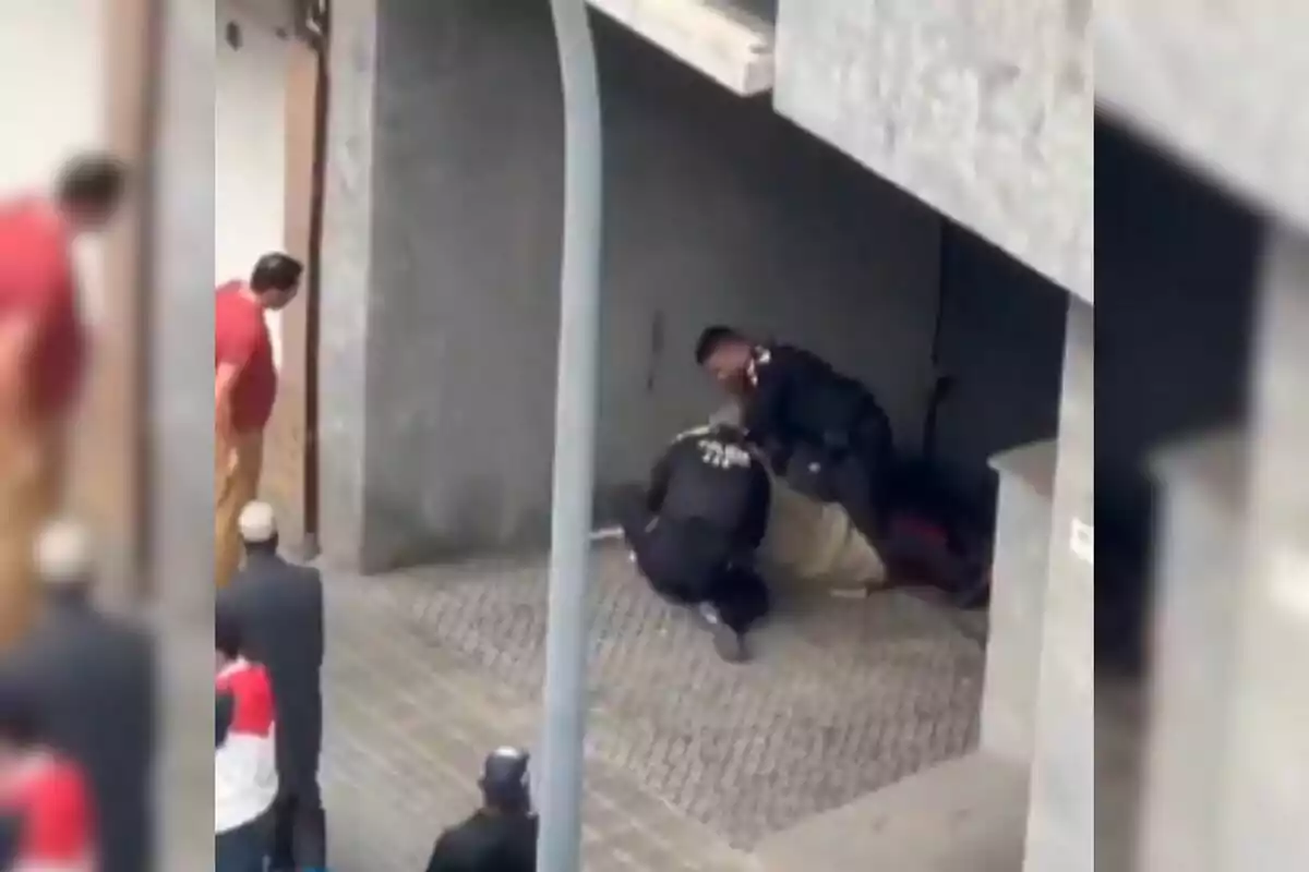 Diverses persones observen mentre dos policies detenen un individu a l'entrada d'un edifici.