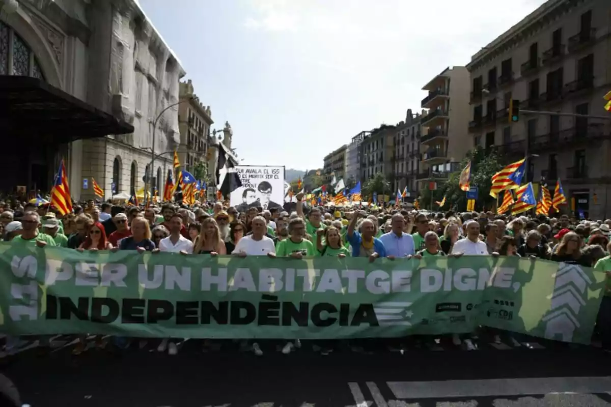 Una multitud de persones marxant en una manifestació amb una pancarta verda que diu "PER UN HABITATGE DIGNE, INDEPENDÈNCIA" i banderes catalanes onejant al fons.