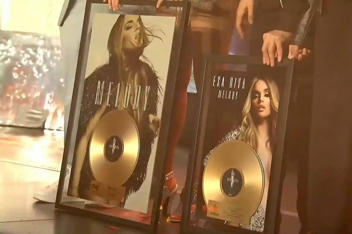 Dues persones sostenen discos d'or emmarcats amb imatges d'una artista femenina a la portada. Dues persones sostenen discos d'or emmarcats amb imatges d'una artista femenina a la portada.