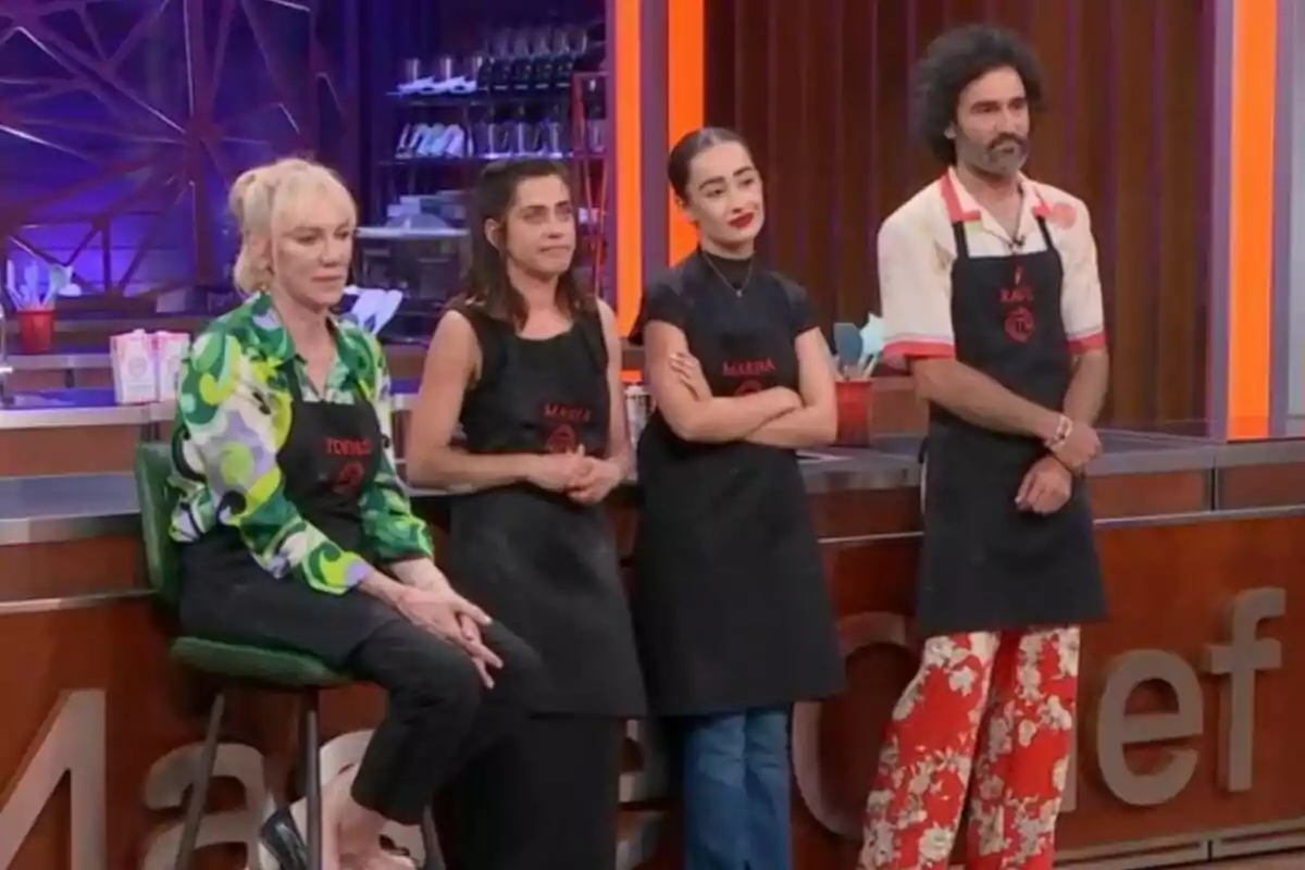 Topazi Fresh, María León, Marina Rivers i Raúl Gómez amb davantals negres estan drets en un set de cuina, amb una decoració moderna i utensilis de cuina al fons a MasterChef Celebrity.