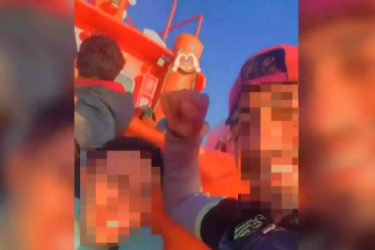 Captura d´un vídeo d´un immigrant en un vaixell amb la cara pixelada, mirant a càmera i amb gorra, alçant el puny dret