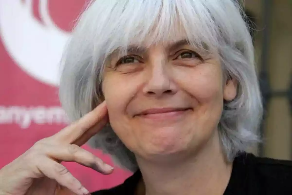 A person with short gray hair smiling in front of a pink background.