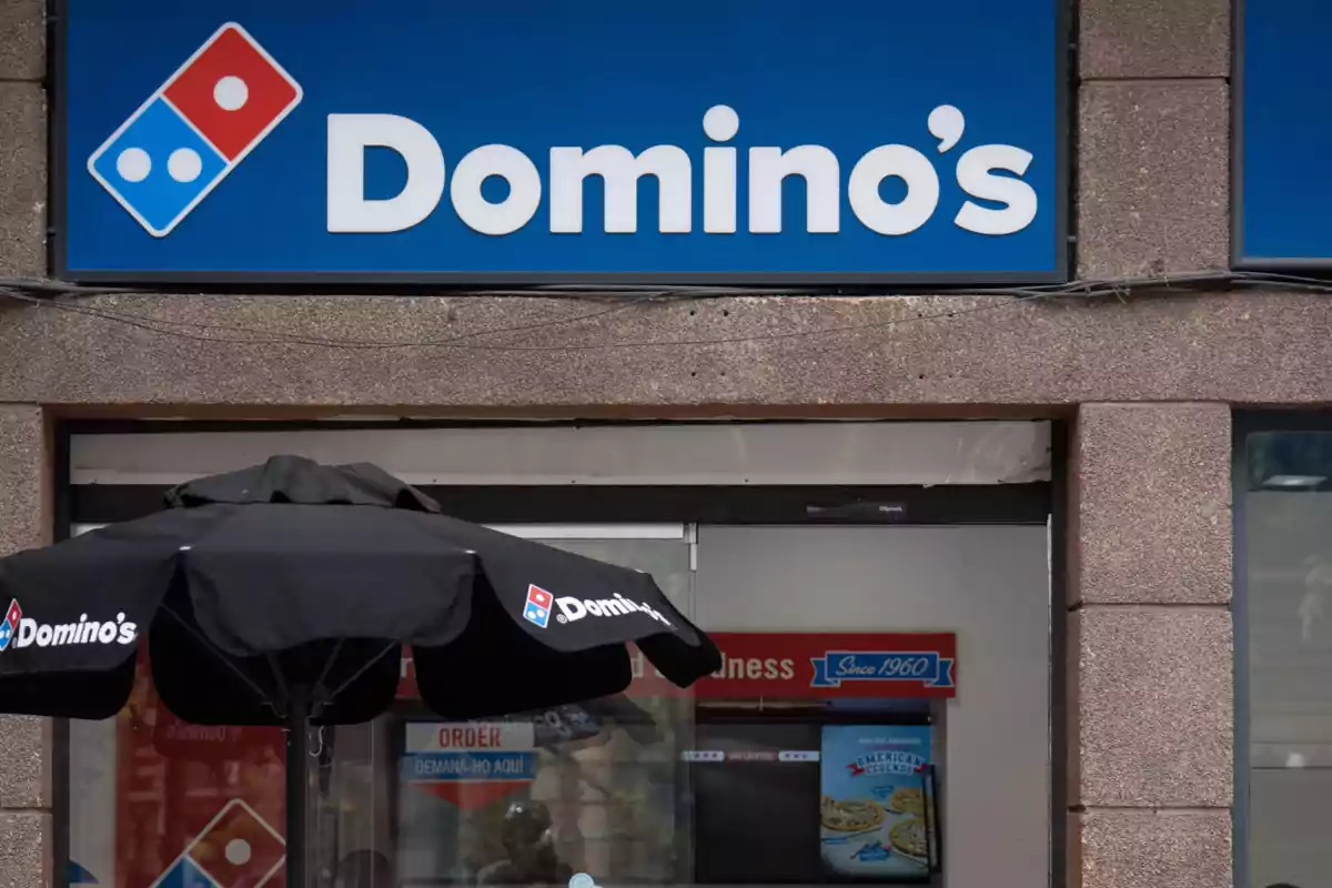 Façana d'una pizzeria amb el logotip de Domino's i un tendal negre.