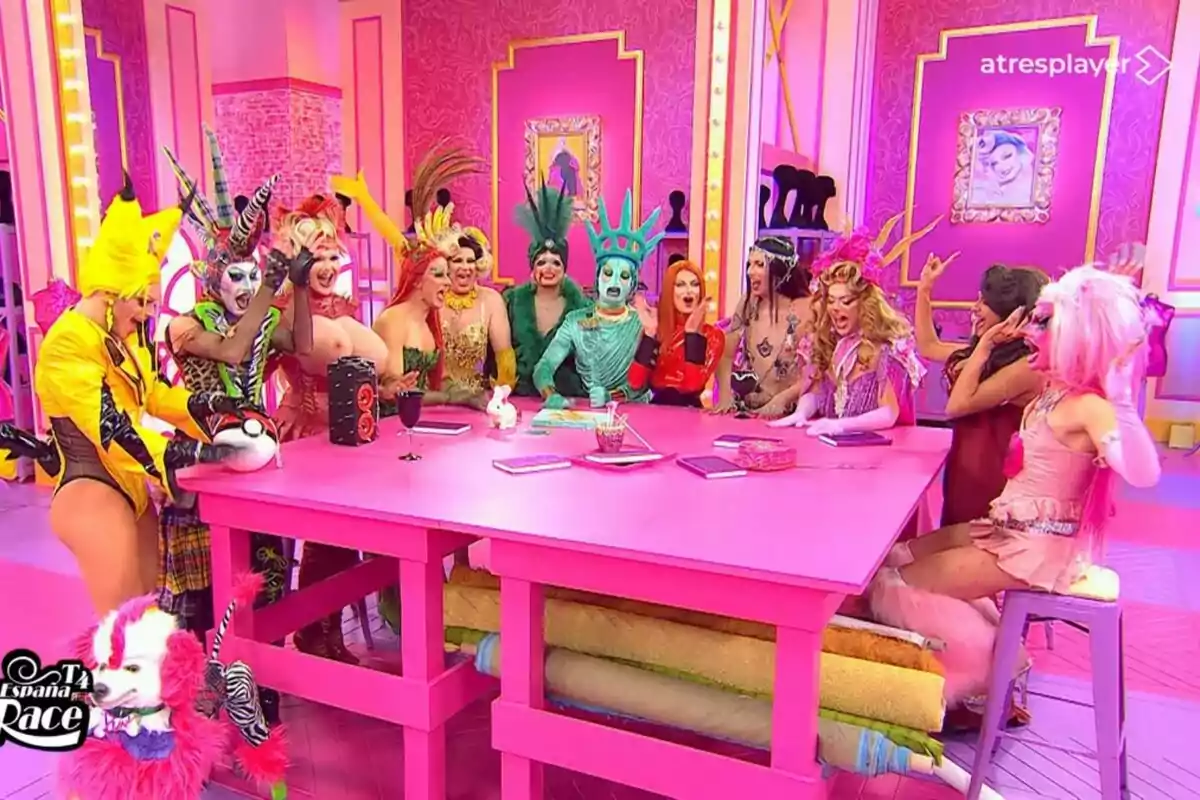 Les reines amb disfresses colorides i extravagants estan reunides al voltant d'una taula rosa en un set de televisió decorat amb tons rosats i detalls daurats a Drag Race España.