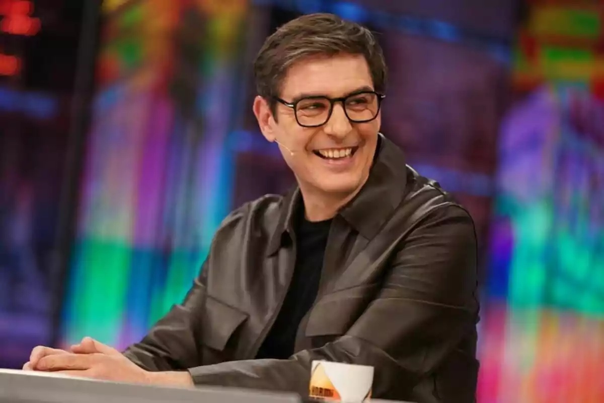 Juanra Bonet amb ulleres i jaqueta fosca somriu mentre està assegut a 'El Hormiguero'.