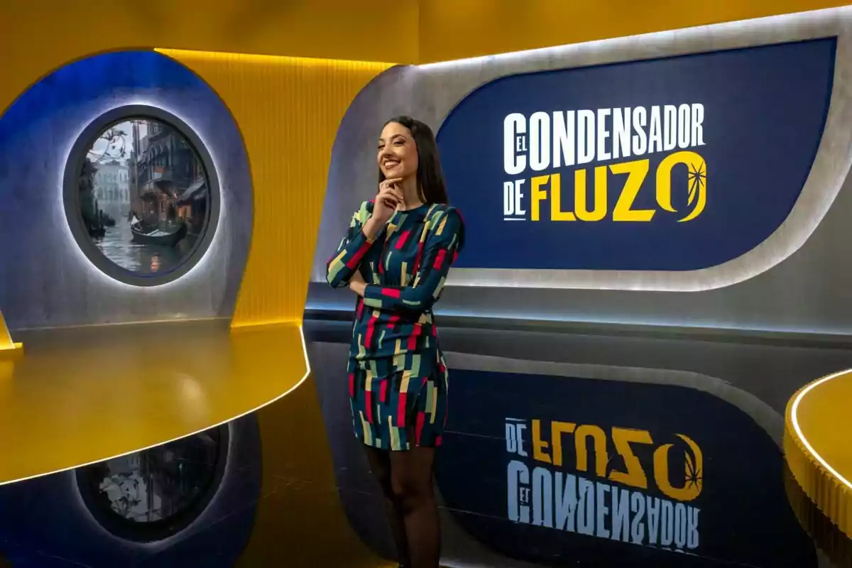 Maya Pixelskaya somrient en un set de televisió amb un disseny modern i colorit, amb un rètol que diu Maya Pixelskaya somrient en un set de televisió amb un disseny modern i colorit, amb un rètol que diu