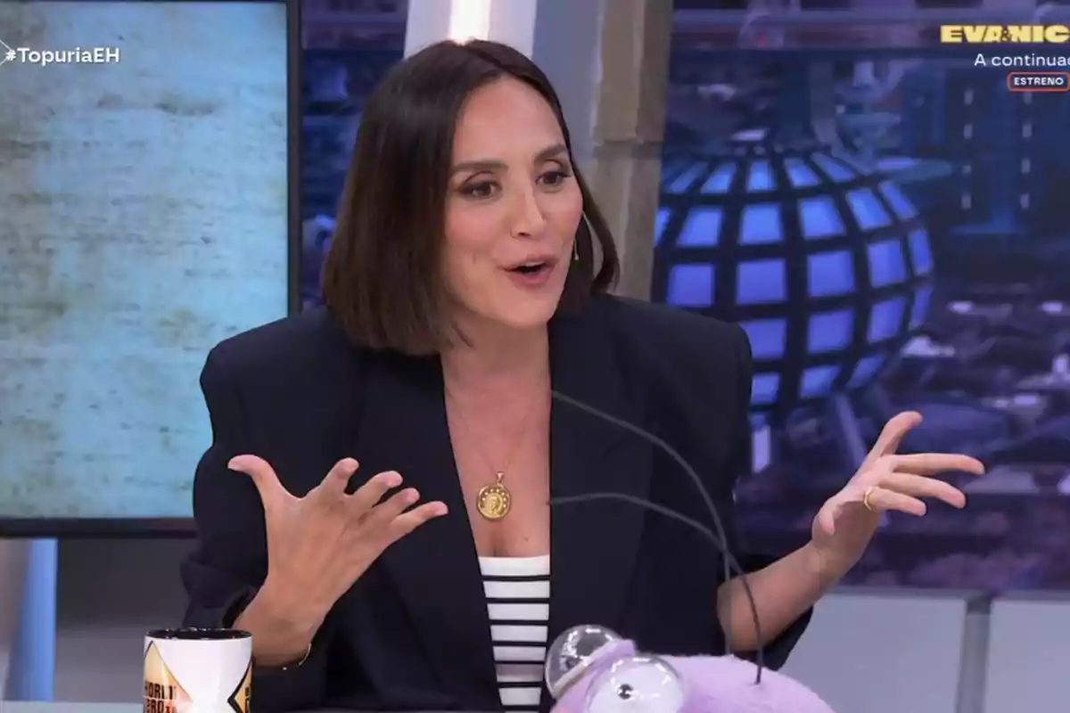 Tamara Falcó està gesticulant mentre parla en un programa de televisió, porta un collaret daurat i una jaqueta fosca, i hi ha una tassa i un objecte morat a la taula davant d'ella. Captura de 'El Hormiguero'.