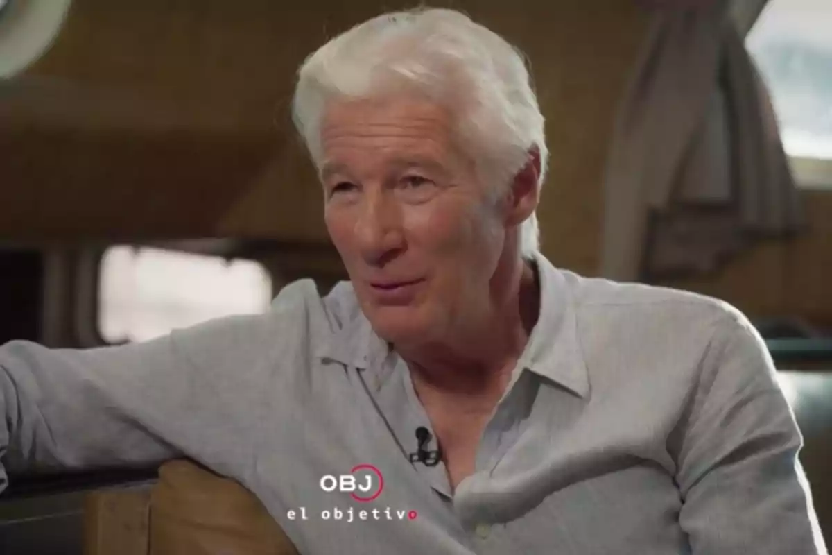 Richard Gere con camisa clara está sentado y hablando en un ambiente interior con cortinas al fondo. Captura de 'El Objetivo' Richard Gere con camisa clara está sentado y hablando en un ambiente interior con cortinas al fondo. Captura de 'El Objetivo'