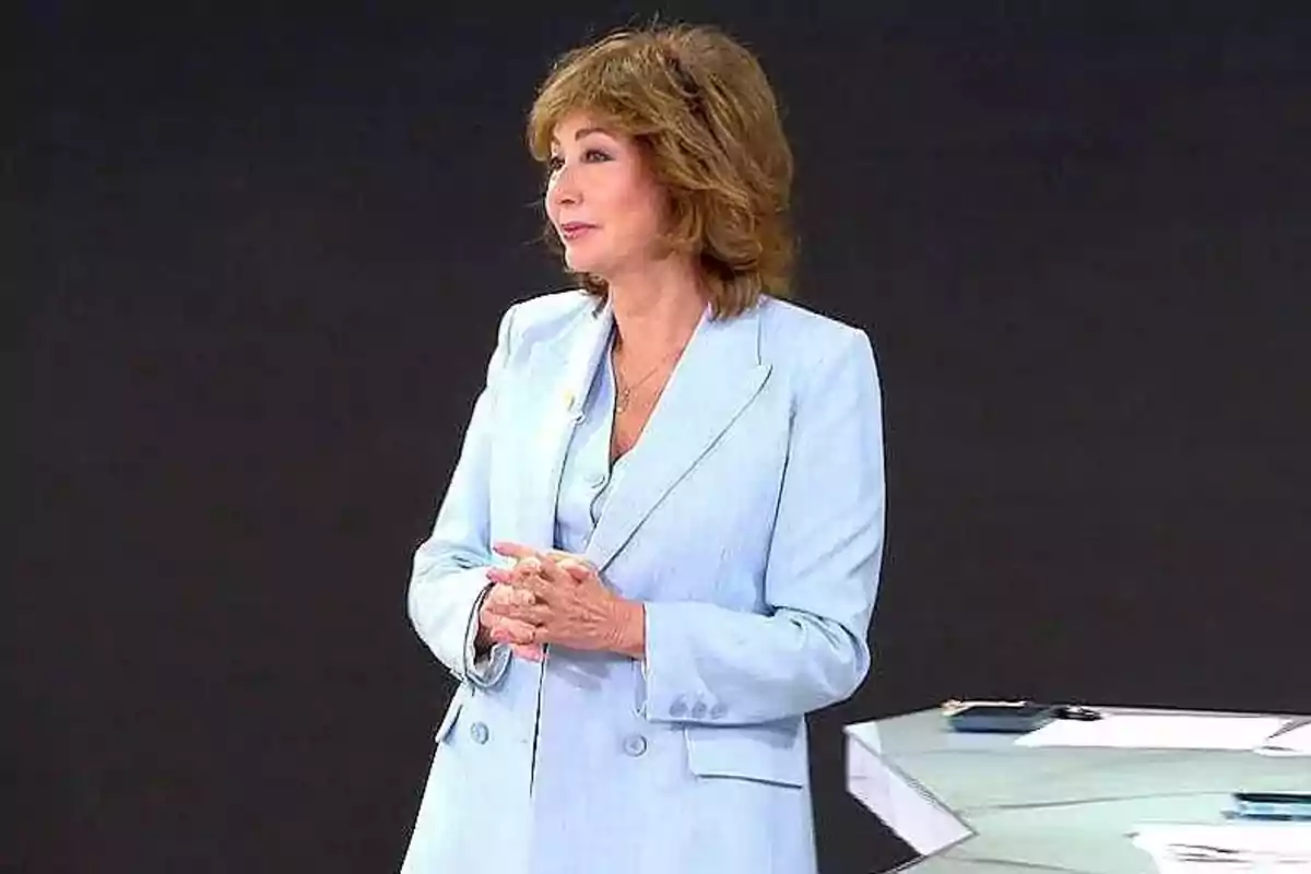 Ana Rosa Quintana amb vestit blau clar dempeus al costat d'una taula en un estudi. Captura de 'El Programa de AR'