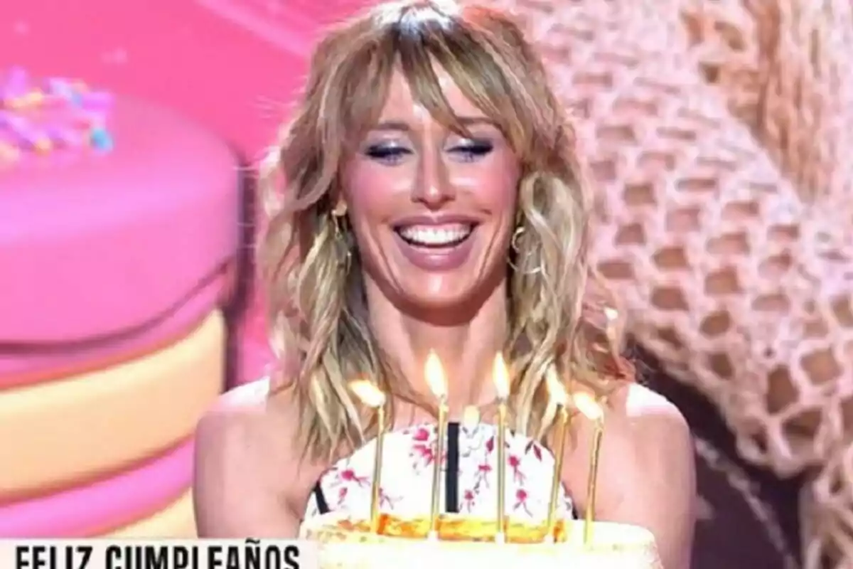 Emma García somrient sosté un pastís d’aniversari amb espelmes enceses davant d’un fons colorit a Festa Emma García somrient sosté un pastís d’aniversari amb espelmes enceses davant d’un fons colorit a Festa