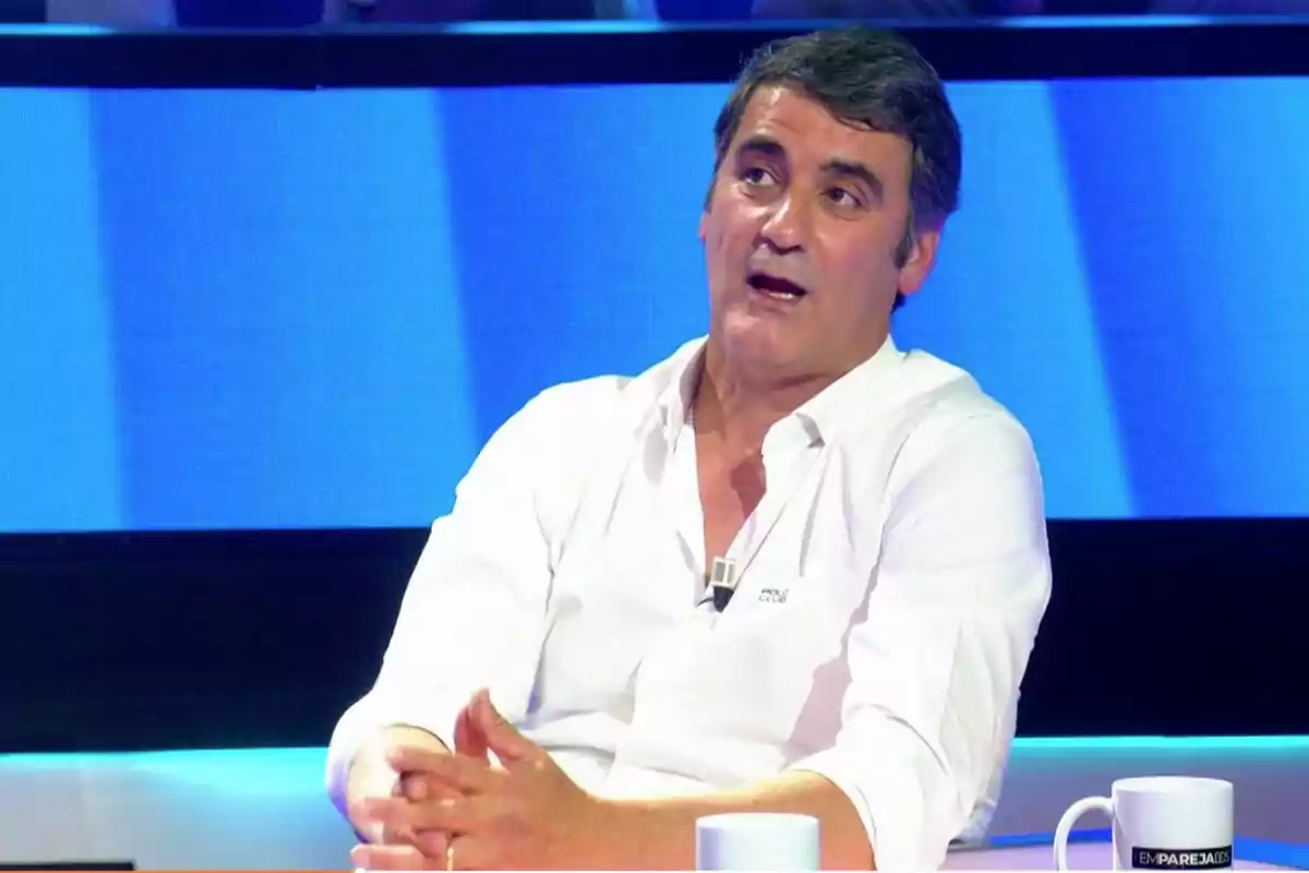 Jesulín de Ubrique amb camisa blanca està assegut a 'Emparejados' amb fons blau i tasses blanques sobre la taula. Jesulín de Ubrique amb camisa blanca està assegut a 'Emparejados' amb fons blau i tasses blanques sobre la taula.