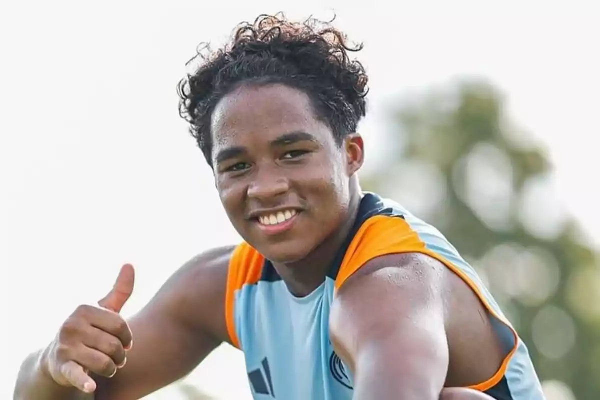 Un jove esportista somriu i fa un gest d?aprovació amb el polze cap amunt mentre porta una samarreta sense mànigues de color blau clar amb detalls taronges. Un jove esportista somriu i fa un gest d?aprovació amb el polze cap amunt mentre porta una samarreta sense mànigues de color blau clar amb detalls taronges.