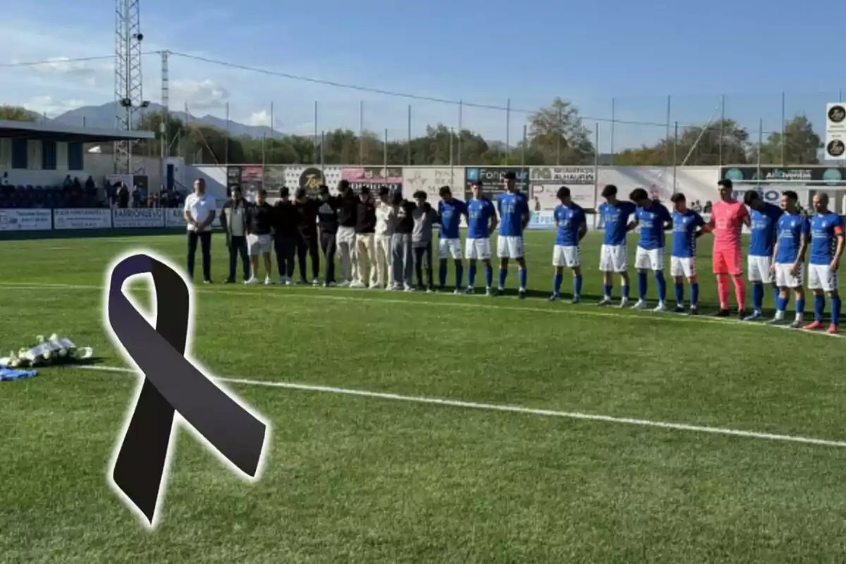 Un equip de futbol i altres persones guarden un minut de silenci al camp, amb un llaç negre en senyal de dol.