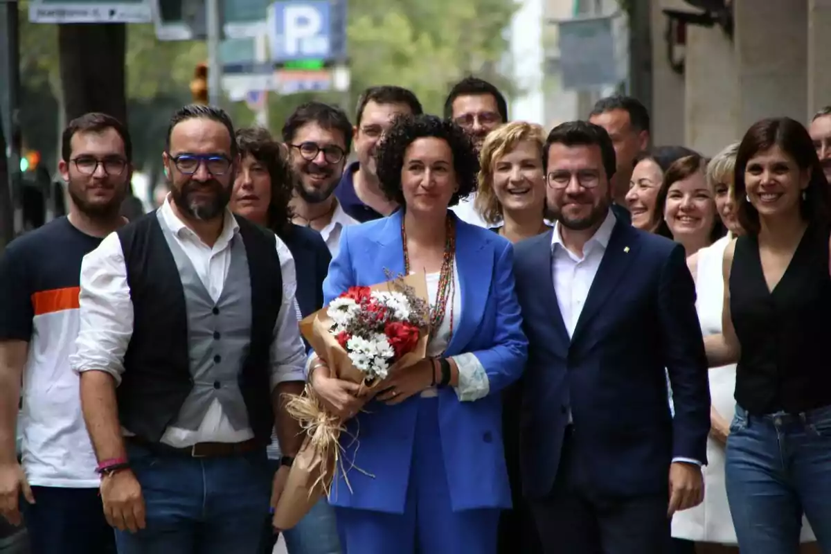 Un grup de dirigents d'ERC somrients posant en un carrer, amb Marta Rovira al centre sostenint un ram de flors.