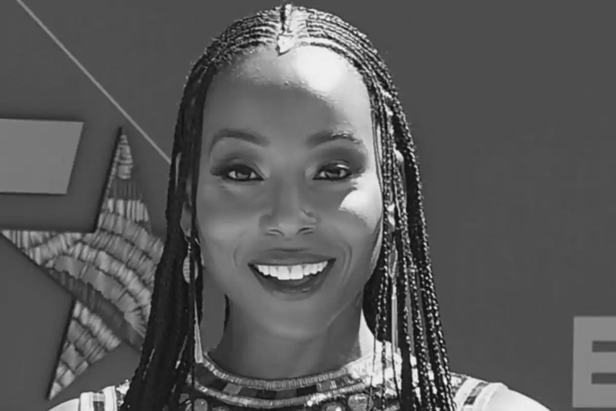 Fotografía en blanco y negro de Erica Ash sonriendo con trenzas y fondo oscuro