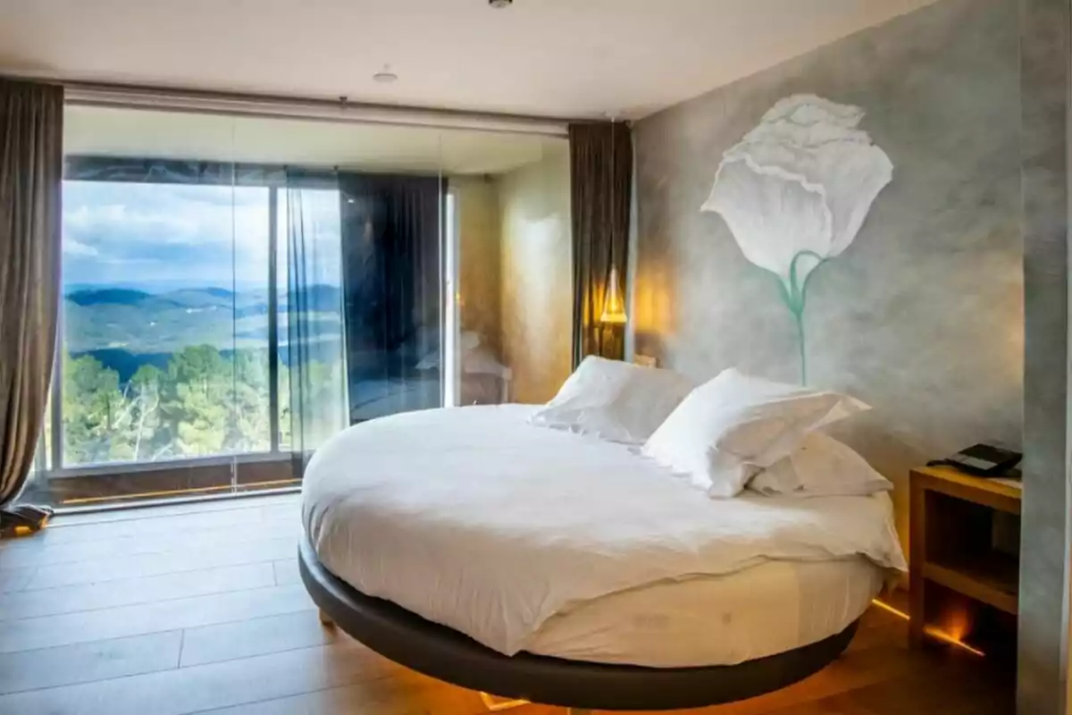 Modern room with a round bed, large window overlooking a mountainous landscape, and a white flower mural on the wall.