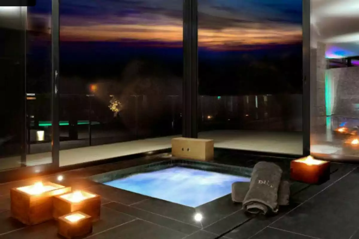 An indoor pool lit by candles and towels in a modern and elegant setting at sunset.