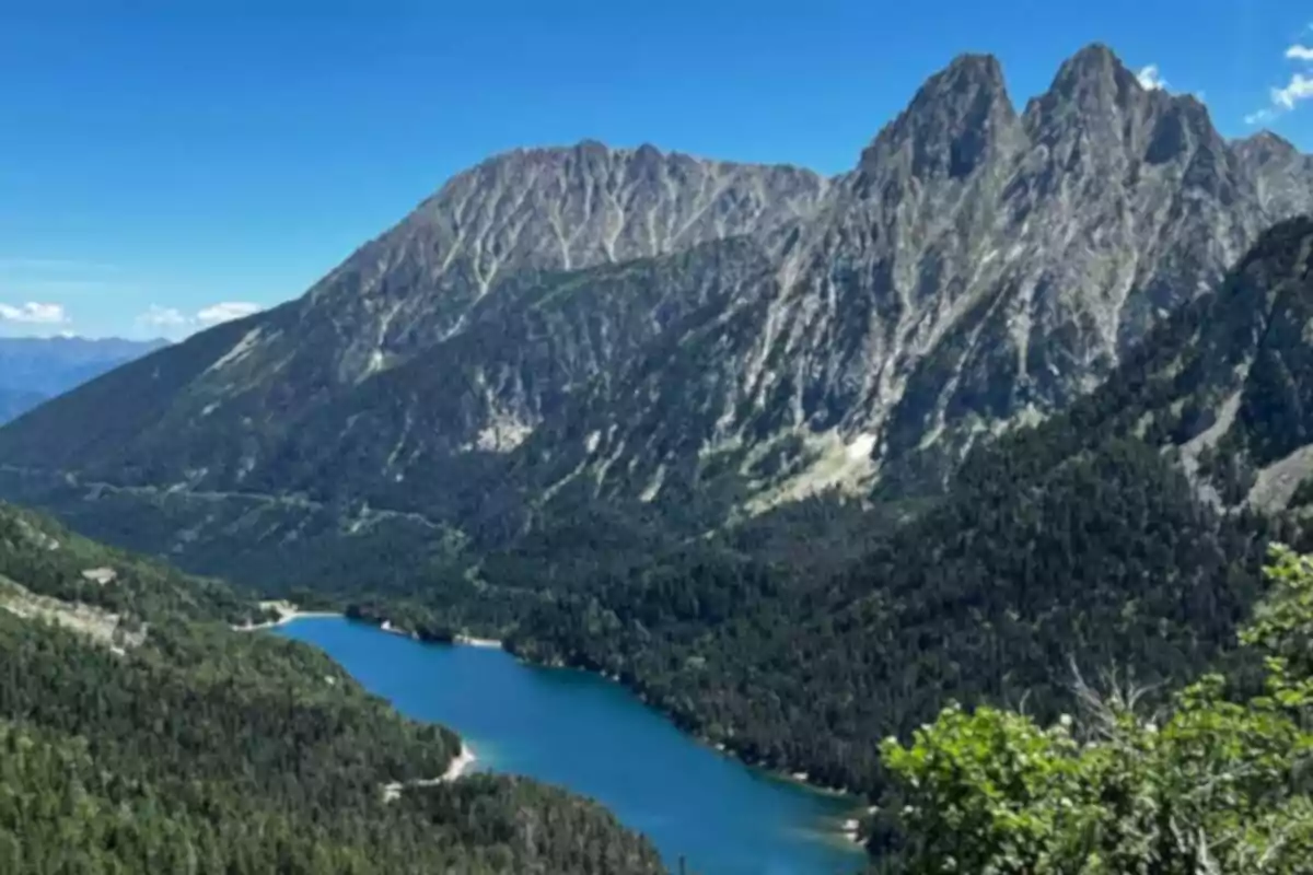 Un lago azul rodeado de montañas y bosques bajo un cielo despejado.