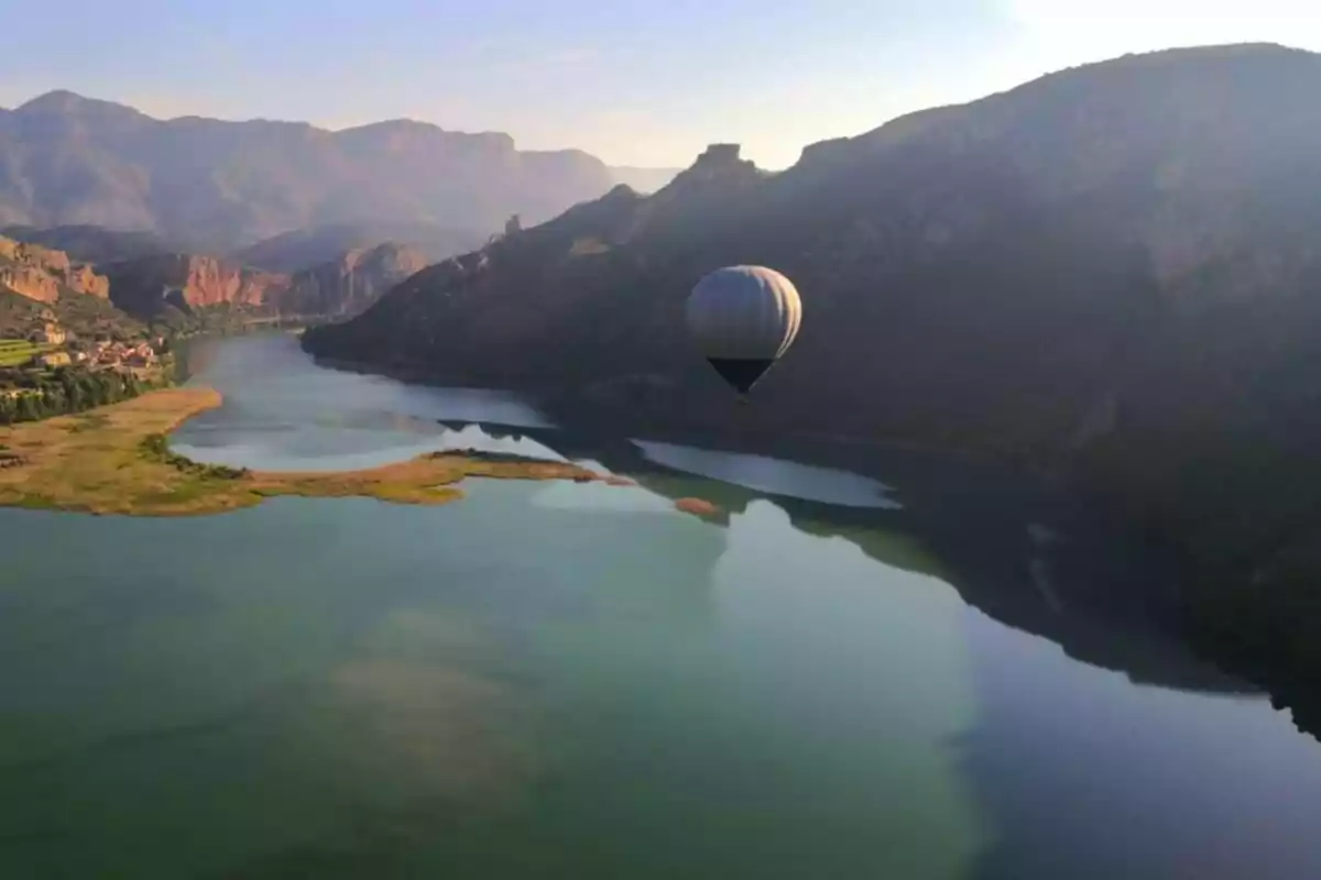 Un globo aerostático sobrevuela un lago rodeado de montañas al atardecer.