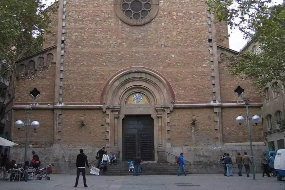 Façana de l'església de Sant Joan Baptista de Gràcia, Barcelona, amb diverses persones caminant davant seu