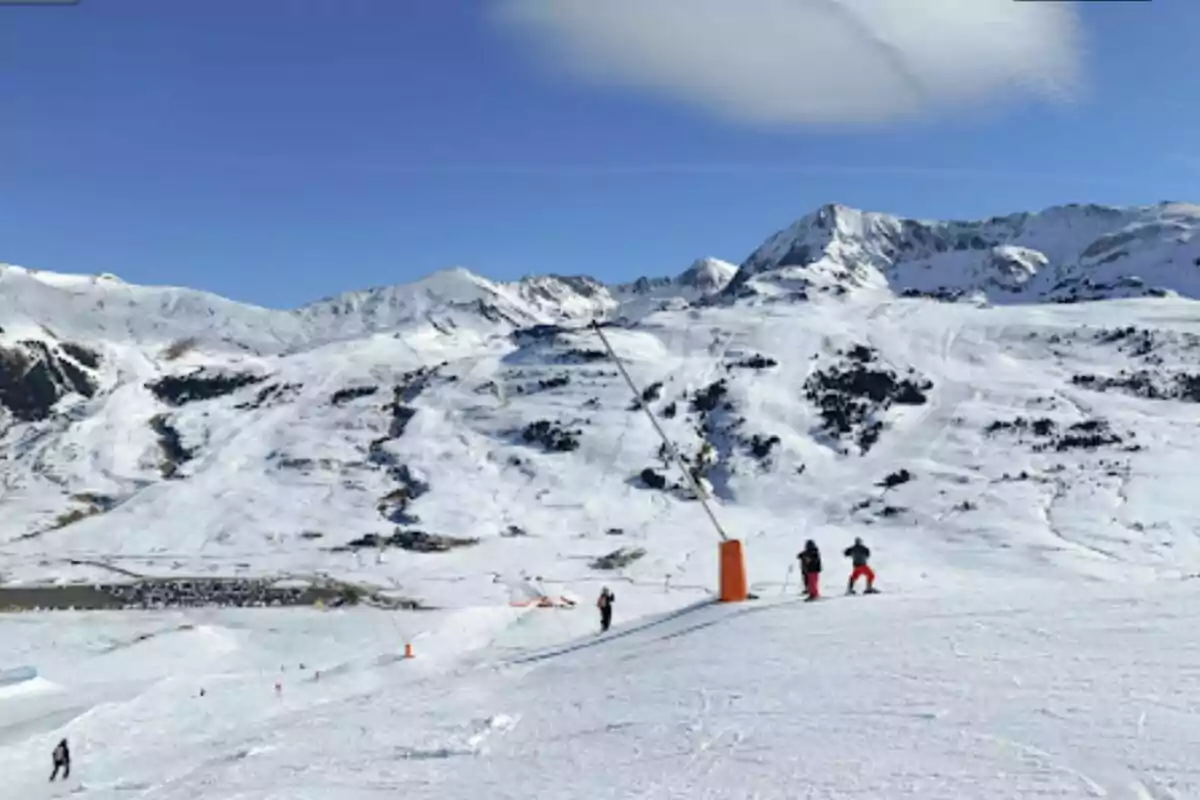 Esquiadores en una pista de nieve con montañas nevadas al fondo bajo un cielo despejado.