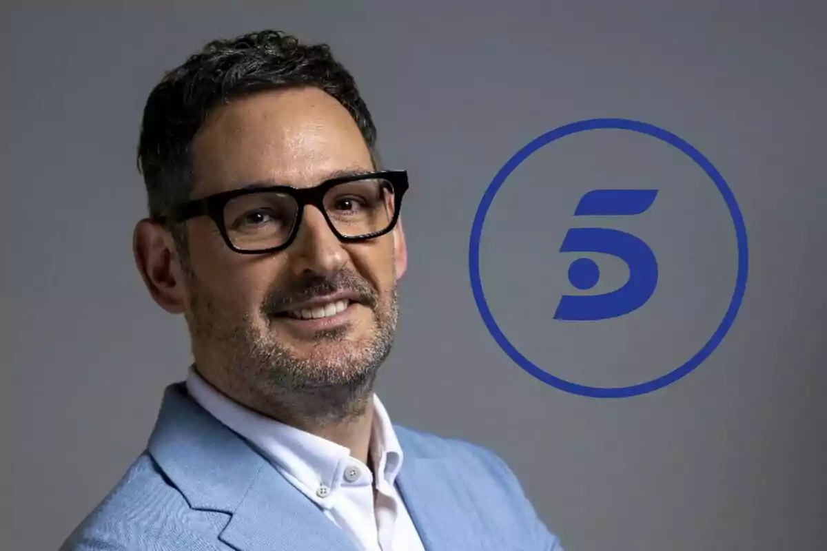Eugeni Alemany amb ulleres i barba somriu vestint una jaqueta blau clar al costat del logotip blau de Telecinco sobre fons gris