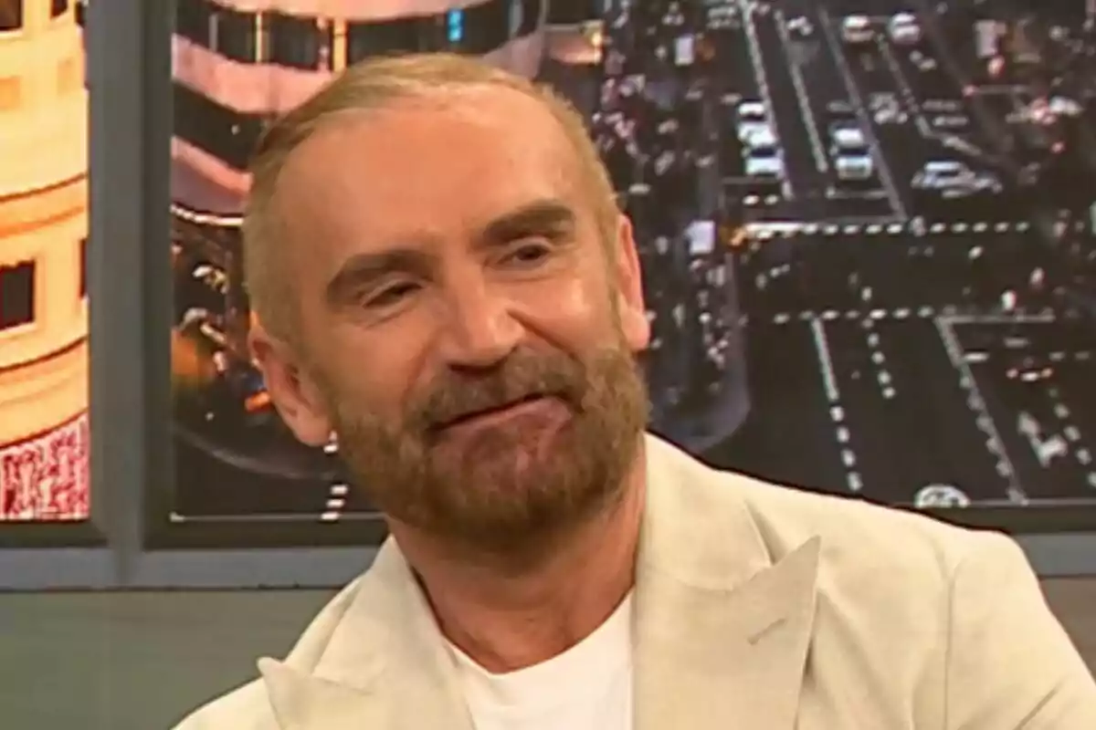 Euprepio Pàdula amb barba i cabell curt porta un vestit clar mentre somriu en un estudi de televisió amb una imatge d'una ciutat de fons a D Corazón. Euprepio Pàdula amb barba i cabell curt porta un vestit clar mentre somriu en un estudi de televisió amb una imatge d'una ciutat de fons a D Corazón.