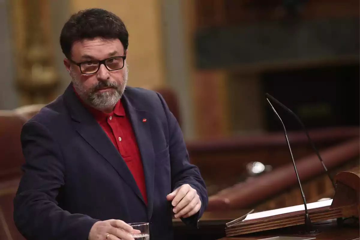 Joan Josep Nuet està dret al faristol del Congrés dels Diputats sostenint un got d'aigua.