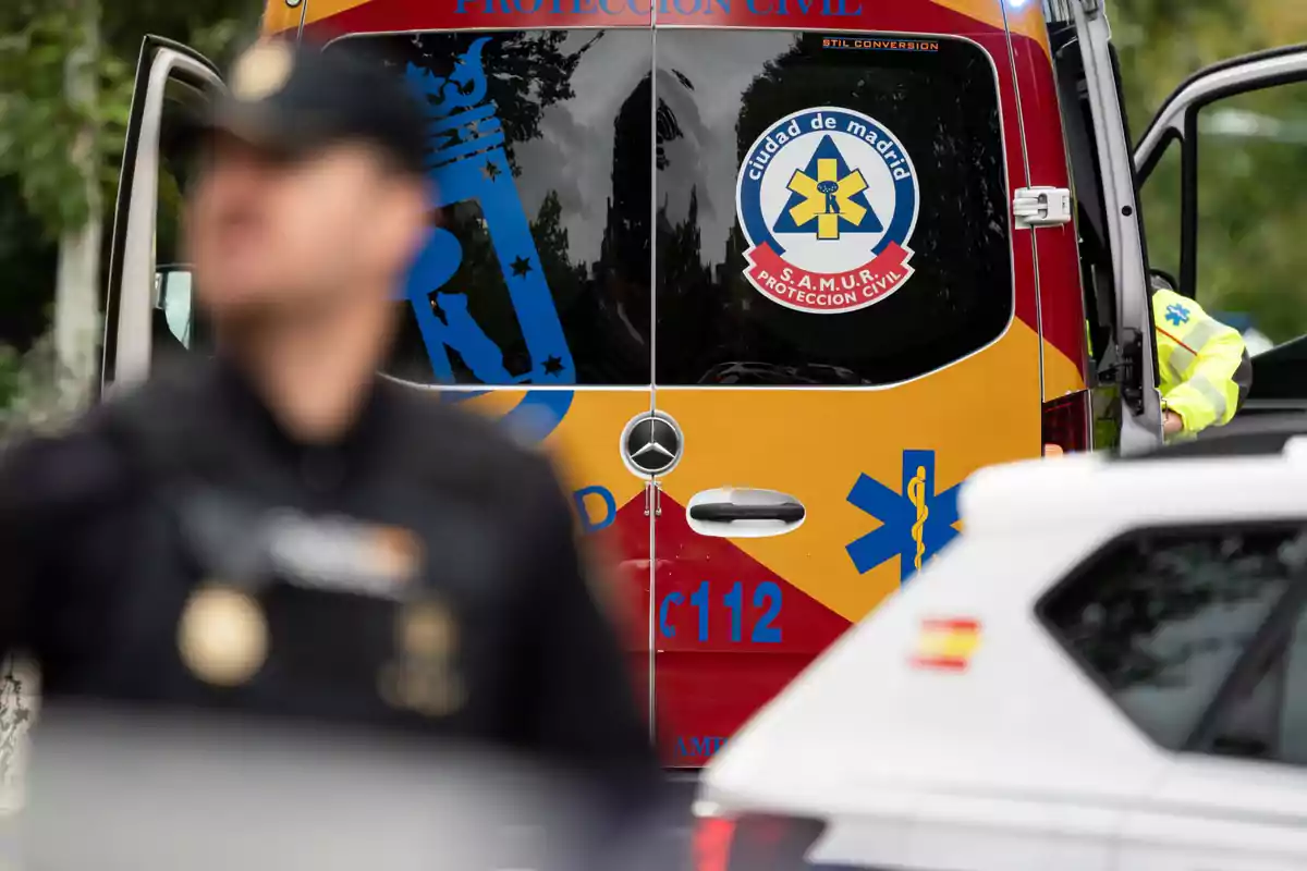 Un vehicle d'emergència del SAMUR de Madrid amb un agent de policia desenfocat en primer pla. Un vehicle d'emergència del SAMUR de Madrid amb un agent de policia desenfocat en primer pla.