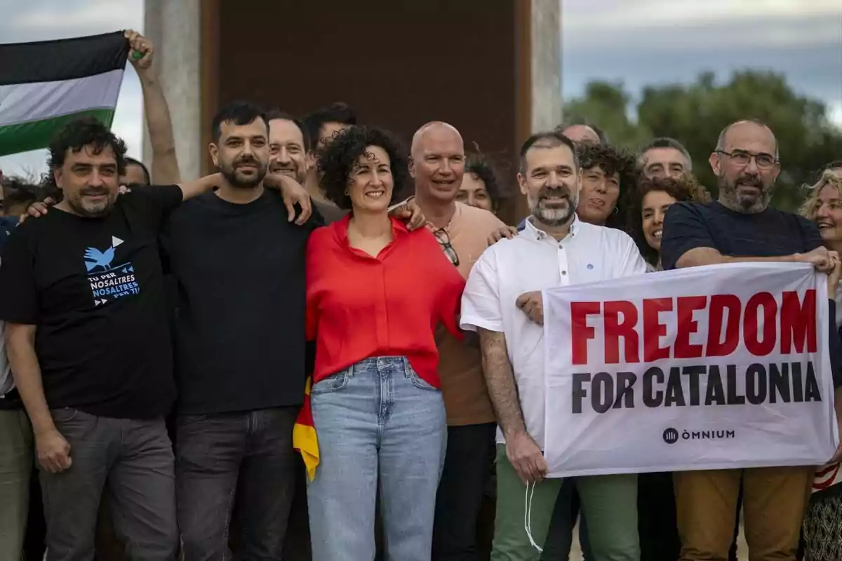 Un grup de persones somrients posant juntes, algunes sostenint una pancarta que diu "FREEDOM FOR CATALONIA" i una bandera al fons.